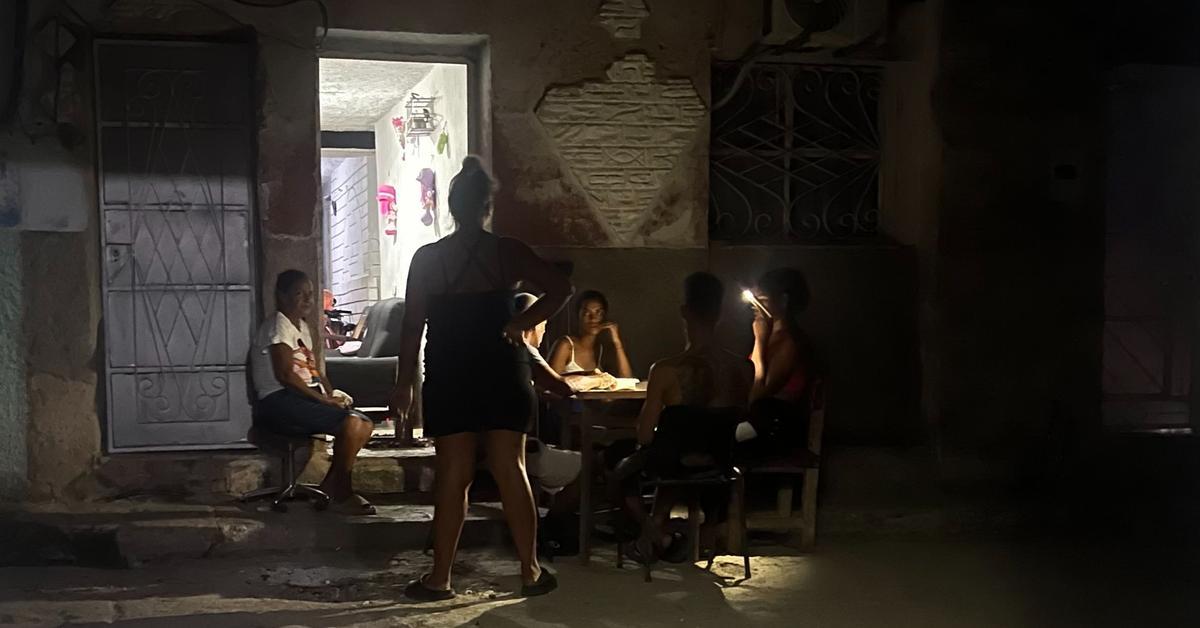 Calle oscura durante un apagón nacional en Cuba con postes y subestación eléctrica en el fondo.